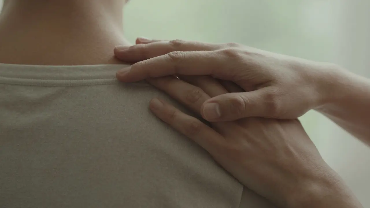 Jemný, terapeutický dotek rukou na zádech symbolizující bezpečí a důvěru bez sexuálních konotací.